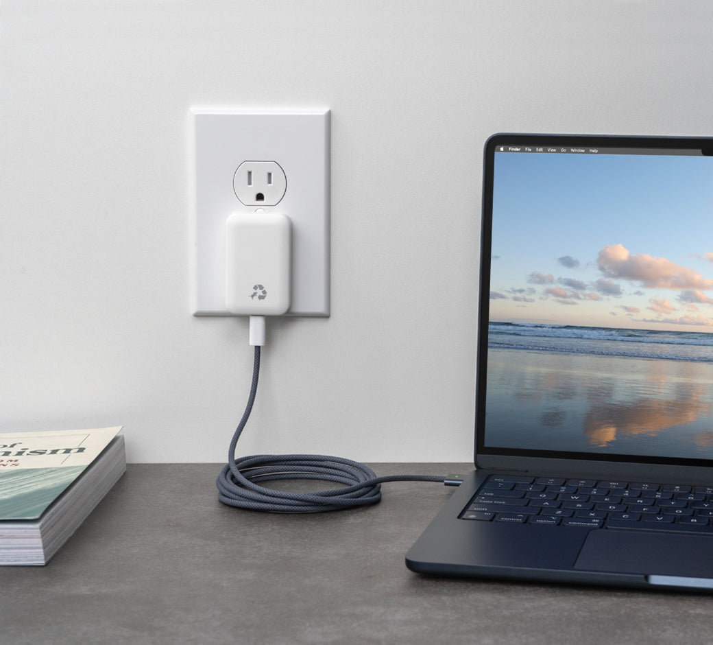 White charger plugged into an outlet, charging a laptop on a desk.