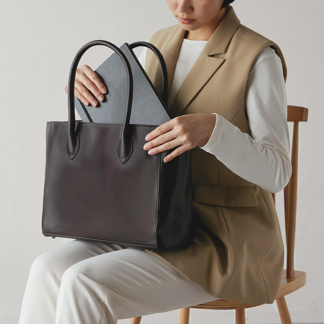 Image of a woman holding an Antique Box Tote in her lap and pulling out a notebook