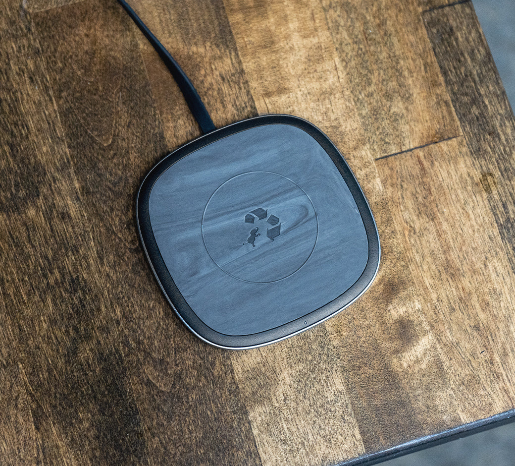 A sleek black wireless charging pad with a marbled surface design placed on a wooden table.