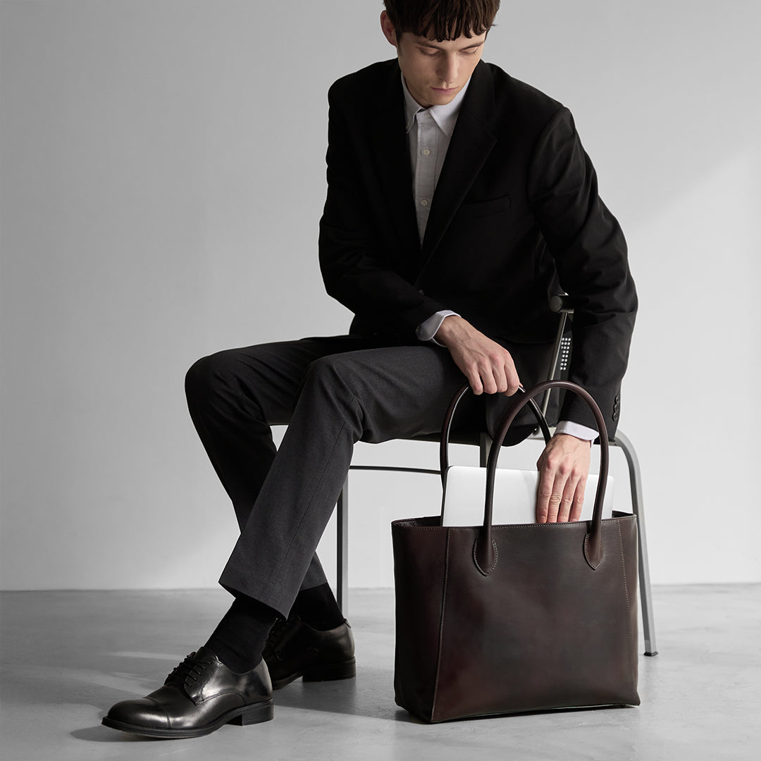 An Antique Career Tote with studs on the ground with a laptop computer inside