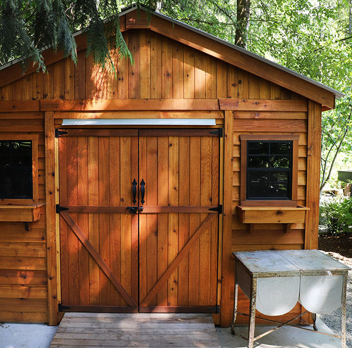 Space Master 12x12 cedar storage shed with double doors, window boxes, and a shingled roof in a backyard setting.