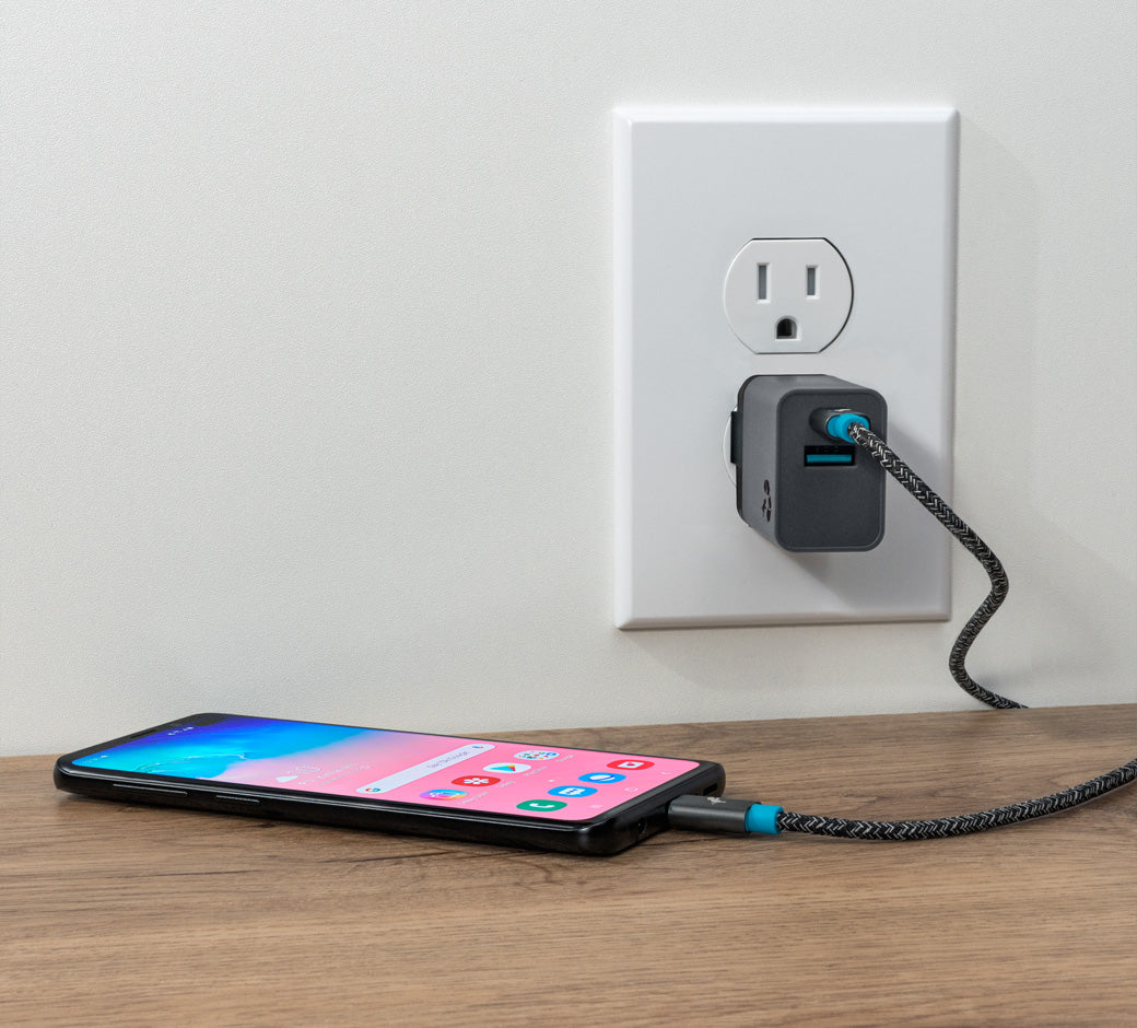USB wall charger with a cable plugged in, charging a smartphone on a wooden surface.