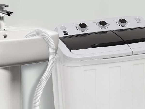 Closeup of Kenmore twin tub washing machine with drain hose hooked over the edge of a pedestal sink. 