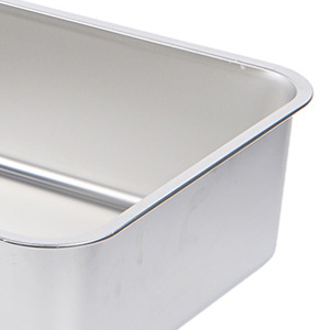 Close-up of a rectangular metal baking pan with rounded corners and a raised edge, shown partially in the frame against a white background.