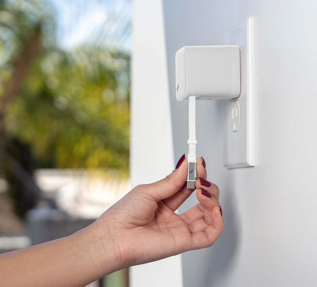 Hand with red nail polish pulling USB-C cable down from White Wall Charger. Window with palm tree blurred in background