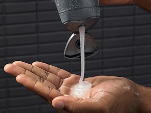 Dove Men+Care Shampoo + Conditioner being poured into hand with black tiles in the background.