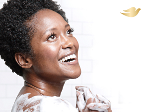 Close-up picture of woman smiling with soap on her shoulder and hands against a white background.
