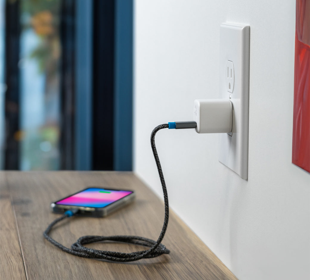White 30W USB-C charger plugged into an outlet charging a smartphone on a wooden side table.
