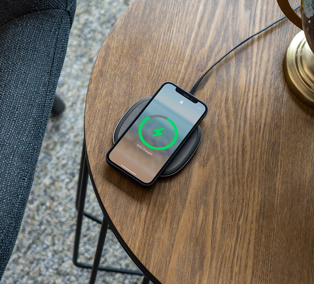 A wireless charger on a wooden table charging a smartphone with a visible green charging indicator.