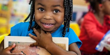 A smiling pre-school student clutches a book to her chest at the Early Steps for School Success program (ESSS) in Barnwell, South Carolina: Photo credit: Susan Warner/Save the Children, October 2014.