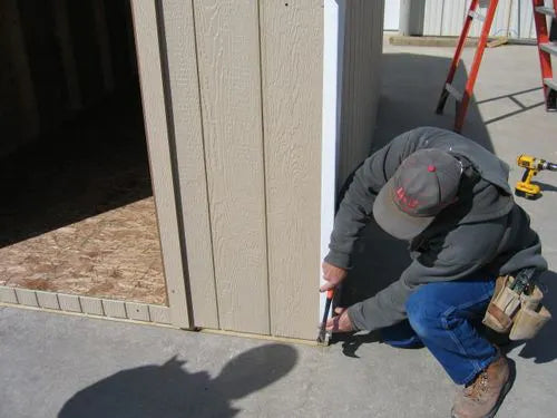 a man installing a trim on the corner of a Little Cottage Company storage shed.