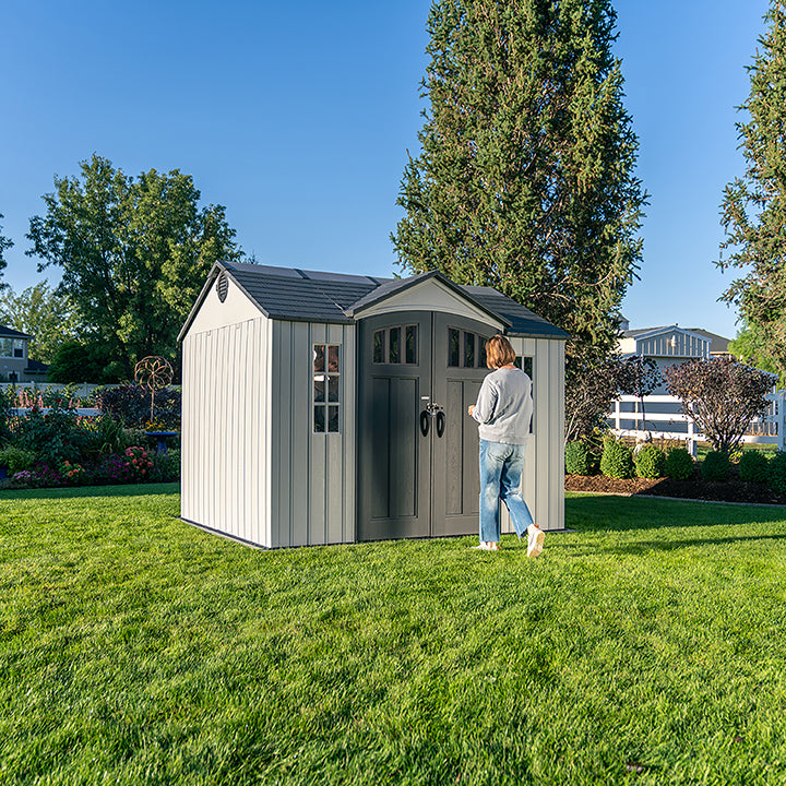 Person walking towards the Lifetime Shed Classic 10 x 8 with closed double doors, set in a beautiful garden.
