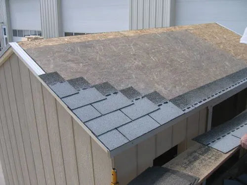 a close up of the roof of a little cottage co storage shed with shingles being installed