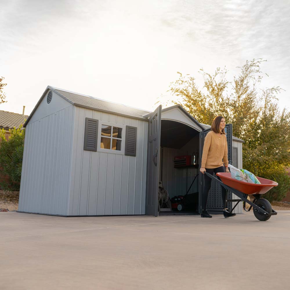 A person carrying a wheelbarrow outside the Lifetime 15x8 Shed, demonstrating the spaciousness and functionality of the shed.