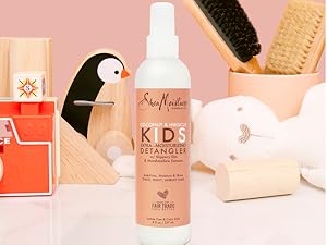SheaMoisture Kids Detangler bottle on a pink surface with kids' toys and combs in the background.