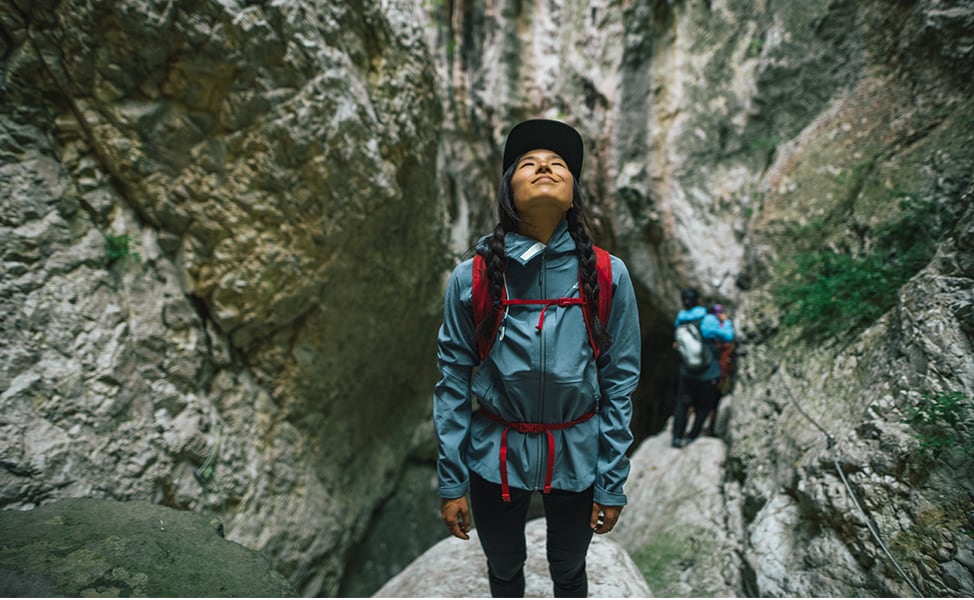 Woman stands on a rocky cliff and gazes skyward.