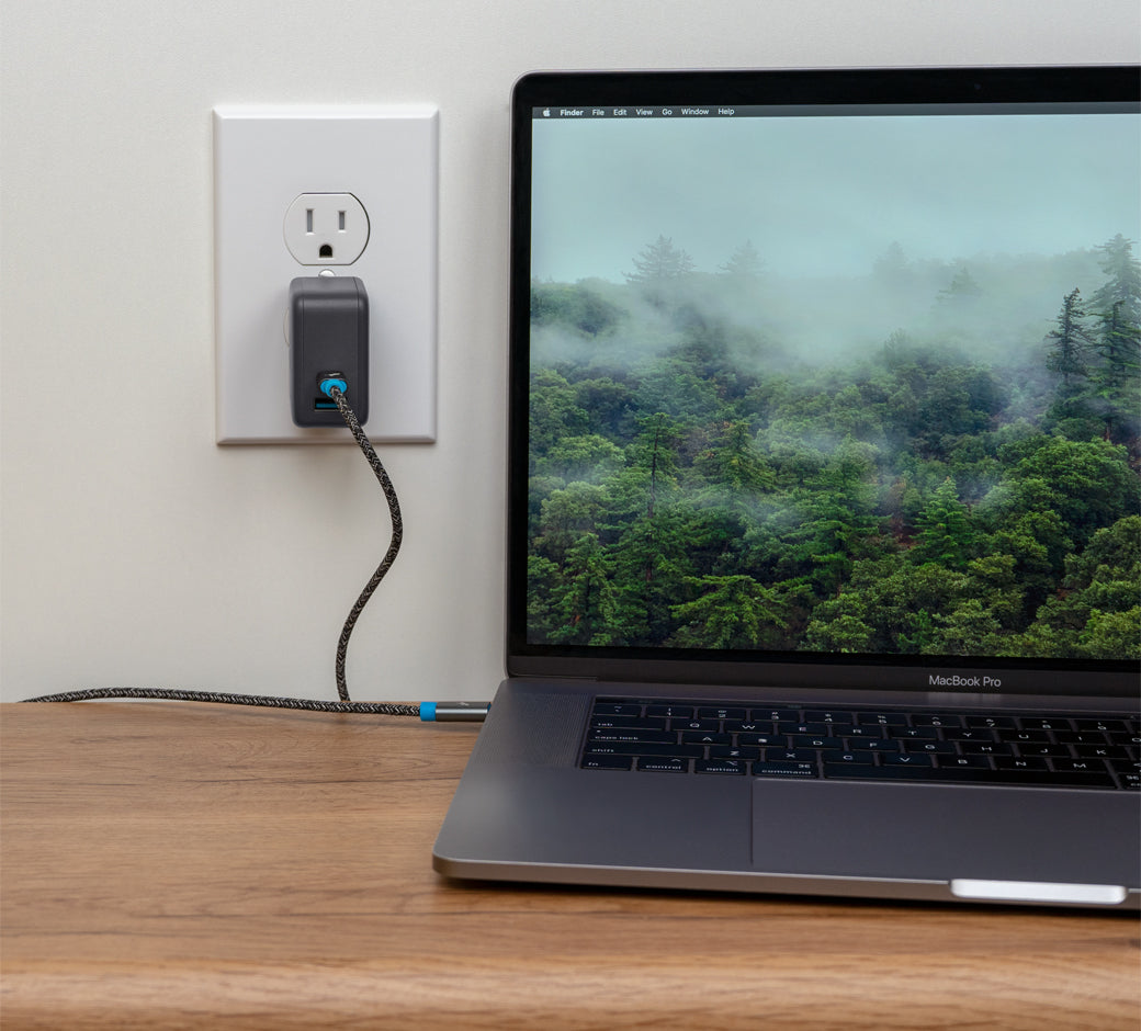Laptop connected to a wall charger with a scenic forest background on the screen.