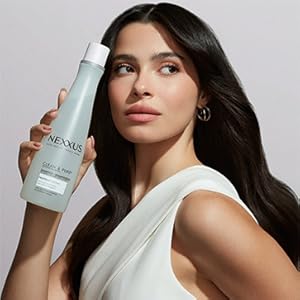 Brown-skinned woman in white dress, black hair, holds Nexxus product against gray background.