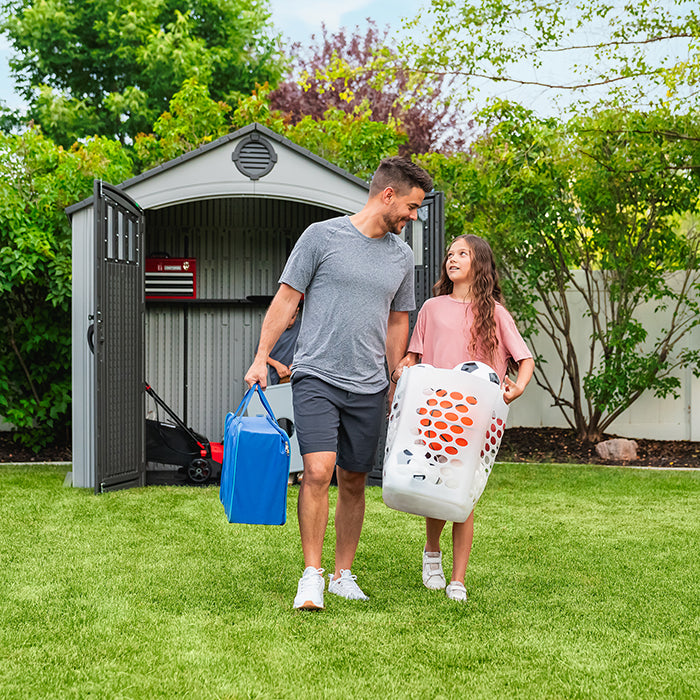 Father and daughter carrying items away from the open Lifetime Classic 8x5 Outdoor Shed in a backyard setting.