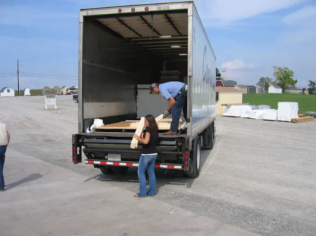 A woman unloading the final piece of a Little Cottage Co storage shed from the delivery truck.
