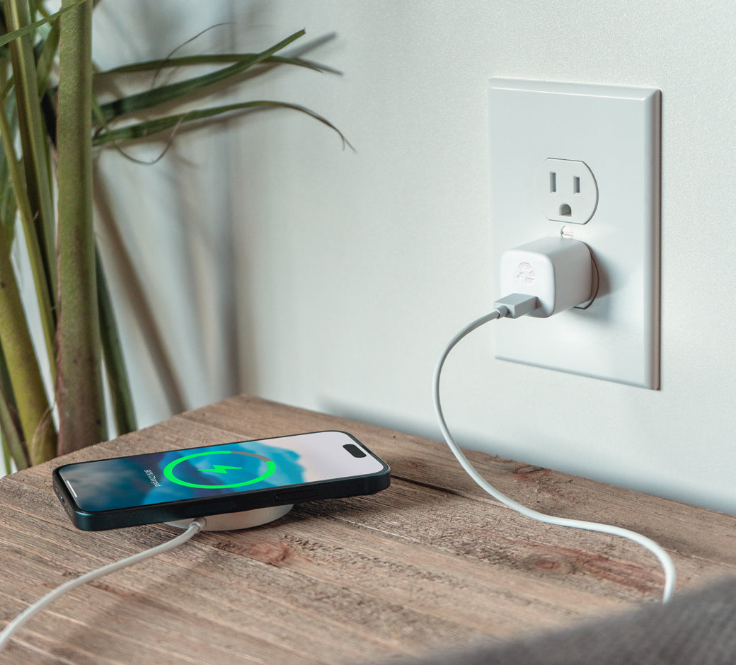 White 30W USB-C charger plugged into an outlet charging a smartphone on a wooden side table.