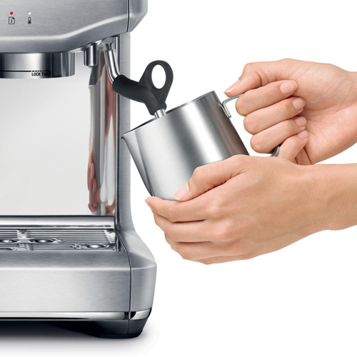 Hands holding a jug against the machine wand.