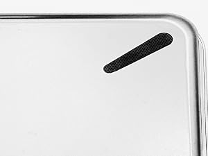 Close-up of a white electronic device corner, showing a black oval-shaped speaker or microphone grille embedded in the surface.