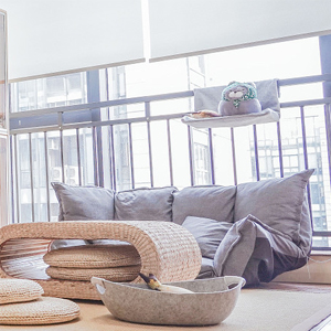 Modern living room with large windows, gray cushions, and woven furniture. Bright, minimalist decor style.