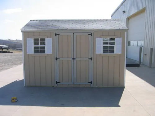A fully assembled Little Cottage Co. wooden storage shed stands on a concrete floor and is ready for painting.