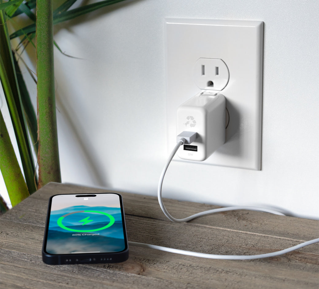 White wall charger plugged into an outlet, charging a smartphone on a desk.