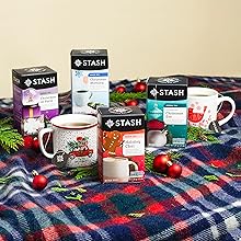 Four stash holiday teas sitting on a blanket with cups of brewed tea